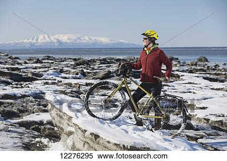 Stock Photography - A young woman stands with her bicycle on ice next to the Tony Knowles Coastal Trail, Anchorage, Southcentral Alaska, USA.. Fotosearch