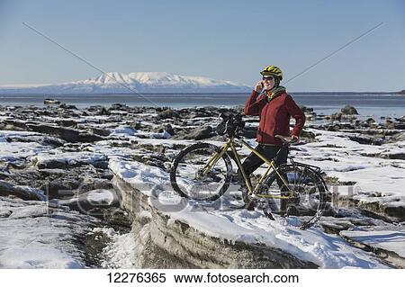 A young woman stands with her bicycle on ice while talking on a cell phone next to the Tony Knowles Coastal Trail, Anchorage, Southcentral Alaska, USA. View Large Photo Image Stock Photography - A young woman stands with her bicycle on ice while talking on a cell phone next to the Tony Knowles Coastal Trail, Anchorage, Southcentral Alaska, USA.. Fotosearch