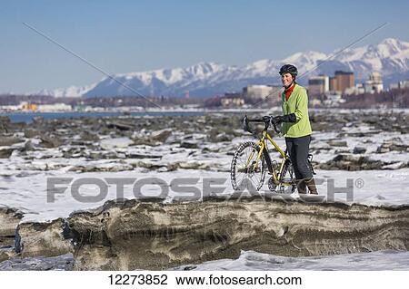 Stock Image - A young woman stands with her studded tire bicycle amongst the ice chunks in the Cook Inlet next to the Tony Knowles Coastal Trail, Anchorage, Southcentral Alaska, USA.. Fotosearch