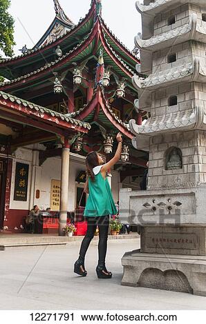 Stock Image - A young woman tries her good luck by throwing a coin into a small window of this tower, Nan Pu Tuo Temple; Xiamen, Fujian Province, China. Fotosearch