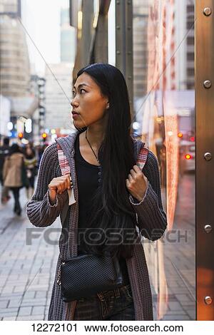 Stock Image - A young woman walking along the street and shops, Kowloon; Hong Kong, China. Fotosearch