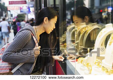 Stock Image - A young woman window shopping at the retail shops along the street, Kowloon; Hong Kong, China. Fotosearch