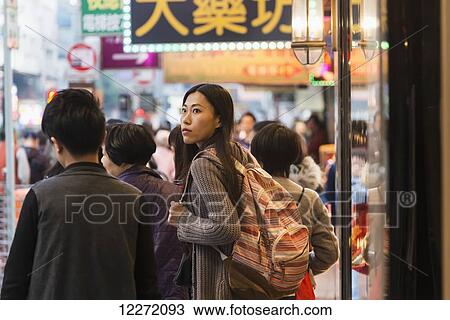 Stock Image - A young woman with backpack among many pedestrians along the busy streets of Kowloon; Hong Kong, China. Fotosearch