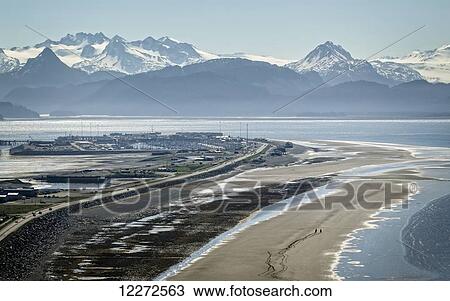 Stock Image - Aerial view of the Homer Spit and Kenai Mountains with horseback riders on the beach, Southcentral Alaska, Spring. Fotosearch