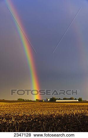 Stock Photo - Agriculture - A brilliant double rainbow forms over a farmstead and field after a Spring storm. The previous year's corn stubble is still present in the field prior to planting / Central Iowa, USA.. Fotosearch
