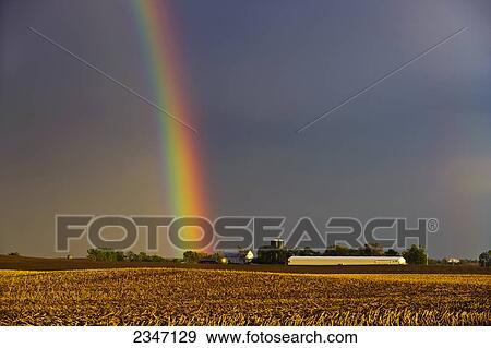 Stock Photo - Agriculture - A brilliant double rainbow forms over a farmstead and field after a Spring storm. The previous year's corn stubble is still present in the field prior to planting / Central Iowa, USA.. Fotosearch