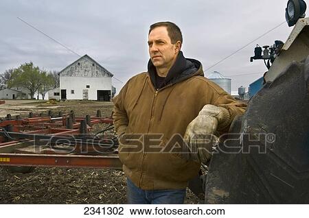 Agriculture - A farmer looks out across his field before beginning cultivating operations on a cold overcast Spring day, with farm buildings in the background / Iowa, USA. View Large Photo Image Stock Image - Agriculture - A farmer looks out across his field before beginning cultivating operations on a cold overcast Spring day, with farm buildings in the background / Iowa, USA.. Fotosearch