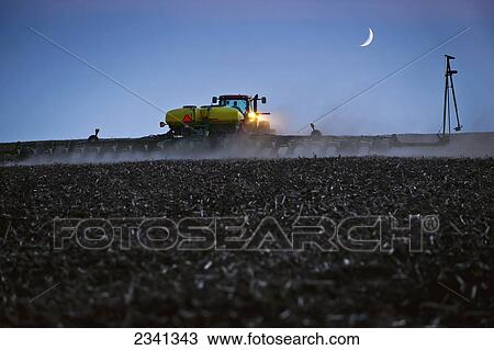 Stock Image - Agriculture - A farmer plants a soybean crop at night with a crescent moon above the field. Corn stubble is left over from the previous year's corn harvest / Central Iowa, USA.. Fotosearch