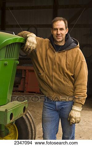 Agriculture - A farmer stands next to his John Deere tractor at the entrance of his workshop prior to spring cultivating and planting / Iowa, USA. View Large Photo Image Picture - Agriculture - A farmer stands next to his John Deere tractor at the entrance of his workshop prior to spring cultivating and planting / Iowa, USA.. Fotosearch