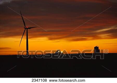 Agriculture - A farmer tills his field at dusk after corn harvest in late Autumn, below an electric wind turbine, illustrating the coexistence of traditional and modern or View Large Photo Image Stock Photo - Agriculture - A farmer tills his field at dusk after corn harvest in late Autumn, below an electric wind turbine, illustrating the coexistence of traditional and modern or. Fotosearch