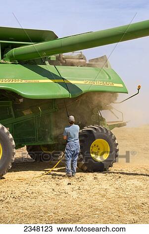 Stock Image - Agriculture - A farmer uses compressed air to blow out the accumulated residue from a combine after a day of harvesting wheat / near Pullman, Palouse Region, Washington, USA.. Fotosearch