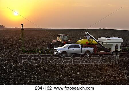 Stock Image - Agriculture - At sunset, a farmer loads bulk soybeans into the hopper of his John Deere 24 row planter during Spring planting operations / Central Iowa, USA.. Fotosearch