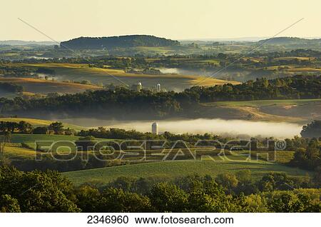 Stock Image - Agriculture - Dairy land at sunrise showing cornfields, alfalfa fields, dairies, silos and fog in low lying areas / Southwest Wisconsin, USA.. Fotosearch