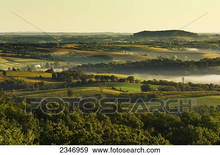 Stock Photo - Agriculture - Dairy land at sunrise showing cornfields, alfalfa fields, dairies, silos and fog in low lying areas / Southwest Wisconsin, USA.. Fotosearch
