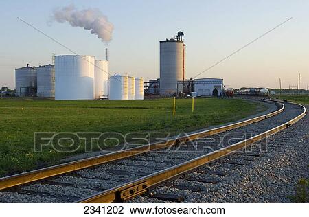 Agriculture - Ethanol production plant showing railroad car access. White ethanol storage tanks on left. Grain silos in background. Steam coming out of the thermal oxidizer stack / Iowa, USA. View Large Photo Image Stock Image - Agriculture - Ethanol production plant showing railroad car access. White ethanol storage tanks on left. Grain silos in background. Steam coming out of the thermal oxidizer stack / Iowa, USA.. Fotosearch