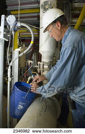 Stock Image - Agriculture - Ethanol production plant. A worker takes a slurry sample from a cooking tank for testing in the laboratory / Iowa, USA.. Fotosearch