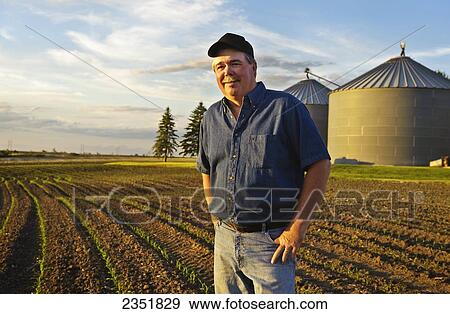 Stock Photo - Agriculture - Portrait of a farmer in his early growth grain corn field several weeks after planting, with grain bins in the background / Central Iowa, USA.. Fotosearch