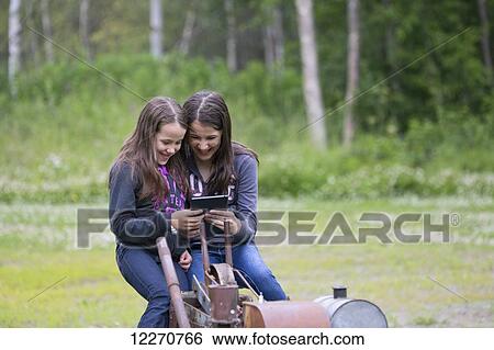 Stock Photograph - Alaska native sisters playing with a smart tablet in Wasilla, Southcentral Alaska, summer.. Fotosearch