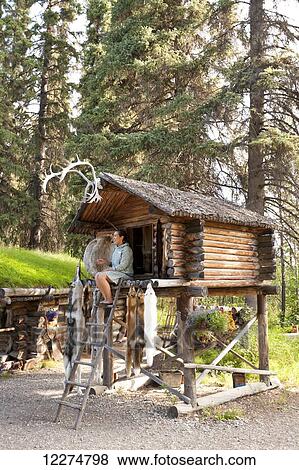 Stock Photo - Alaskan Native Indian guide sitting in a Cache speaking about furs at an Athabascan village on the Riverboat Discovery Tour, Fairbanks, Interior Alaska, Summer. Fotosearch