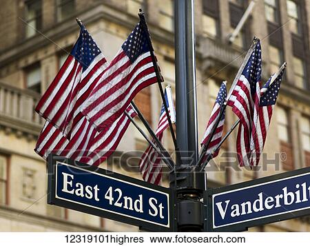 Stock Photograph - American flags on a pole above the street signs at the intersection of East 42nd Street and Vanderbilt; New York City, New York, United States of America. Fotosearch