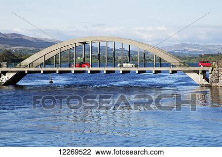 Stock Image - An arched road bridge crossing water with traffic; Kenmare, County Kerry, Ireland. Fotosearch