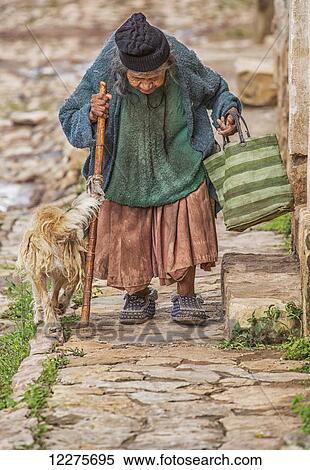 Stock Photography - An elderly woman walks down the cobblestone sidewalk; Toro Toro, Bolivia. Fotosearch