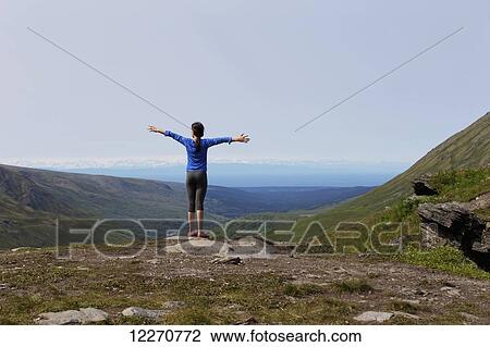 Stock Image - An Inupiat tween girl with outstretched arms looks out over the Talkeetna mountian range, Hatcher Pass, Southcentral Alaska, Summer. Fotosearch
