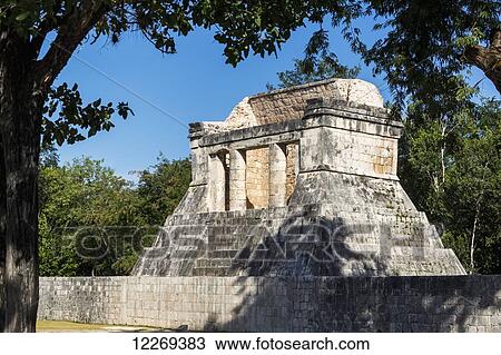 Stock Image - Ancient Mayan Temple with round columns framed by trees and blue sky; Chichen Itza, Yucatan, Mexico. Fotosearch