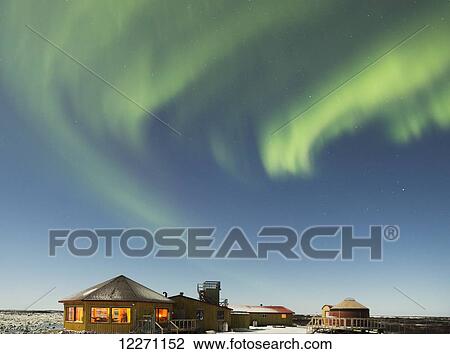 Stock Image - Aurora borealis dancing over top of a building on the Hudson Bay coast line; Manitoba, Canada. Fotosearch