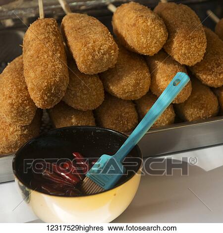 Stock Photograph - Battered meat on a stick with a brush in a bowl of sauce; Seoul, South Korea. Fotosearch