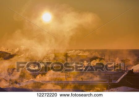 Stock Image - Billowing chimneys of downtown Barrow are silhouetted by the setting sun, Barrow, Arctic Alaska, Winter. Fotosearch