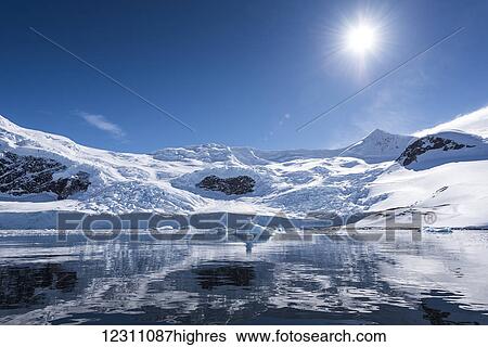 Stock Photograph - Bright sun and snow on the mountains reflected in the water of Neko Harbour; Antarctica. Fotosearch
