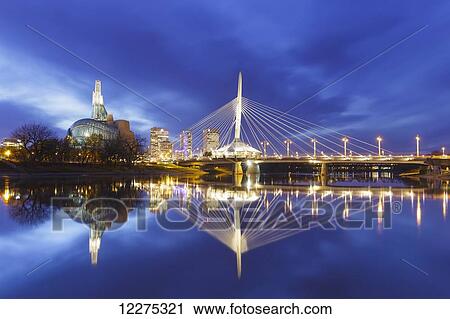 Stock Image - Canadian Museum for Human Rights and Esplanade Riel bridge reflected in the Red River; Winnipeg, Manitoba, Canada. Fotosearch