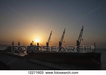 Stock Image - Cargo ship and International navy vessels on anti-piracy duty, Djibouti Port; Djibouti, East Africa. Fotosearch