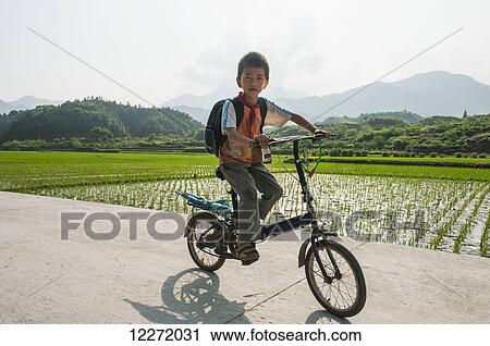 Stock Image - Child riding bike from the scool to home in a small village near Wuyuan; Jiangxi province, China. Fotosearch