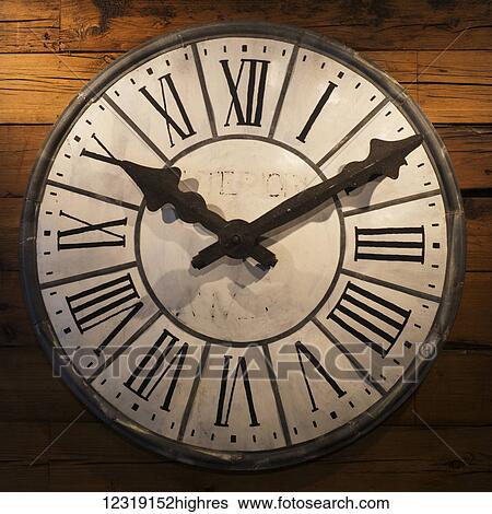 Stock Photograph - Clock with roman numerals and brown hands hanging on a wooden wall; New York City, New York, United States of America. Fotosearch