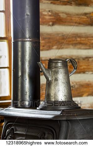 Stock Photograph - Close up of an old metal coffee pot on top of an old cast iron stove in log cabin with window in the background, South of Maple Creek; Alberta, Canada. Fotosearch