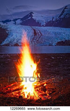 Stock Photography - Close up of campfire in front of Portage Glacier at dusk, Chugach National Forest, Kenai Peninsula, Southcentral Alaska, Summer.. Fotosearch