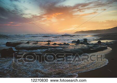 Stock Image - Colourful sunset and water washing up on the shore; Tarifa, Cadiz, Andalusia, Spain. Fotosearch