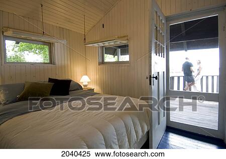 Stock Photography - Cottage Bedroom With A Couple Standing On Balcony, Lake Of The Woods, Kenora, Ontario. Fotosearch