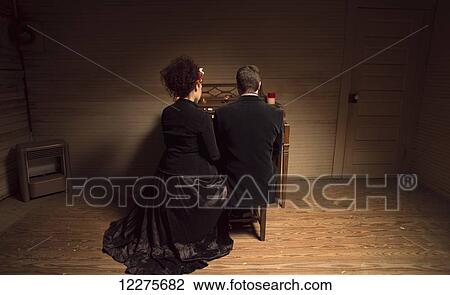 Stock Image - Couple dressed in gothic theme seated at a vintage organ in a run-down church; Pittsboro, North Carolina, USA. Fotosearch