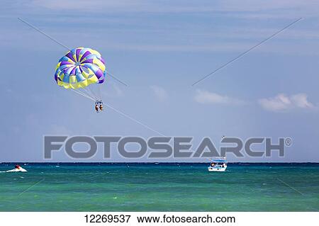 Stock Photo - Couple paragliding attached to boat in the aqua blue water with blue sky; Akumal, Quintana Roo, Mexico. Fotosearch