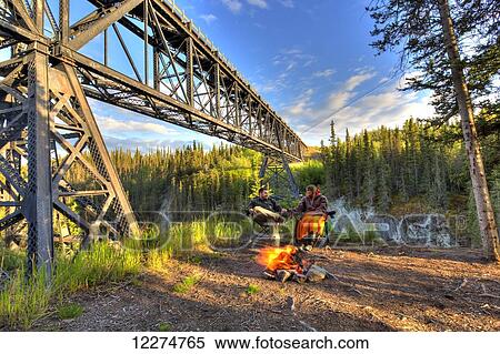 Couple sitting by a campfire holding hands under the Kuskulana River Bridge along the McCarthy Road in Wrangell-St. Elias National Park and Preserve, Southcentral Alaska, Spring, HDR View Large Photo Image Stock Photography - Couple sitting by a campfire holding hands under the Kuskulana River Bridge along the McCarthy Road in Wrangell-St. Elias National Park and Preserve, Southcentral Alaska, Spring, HDR. Fotosearch