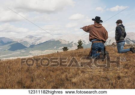 Stock Photograph - Cowboy and a female on their knees looking out towards the rocky mountains, Ya-Ha-Tinda Ranch; Alberta, Canada. Fotosearch
