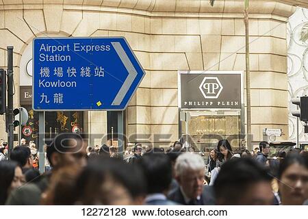 Stock Photo - Crowd in Central district of Hong Kong Island, with a sign for the airport express subway station; Hong Kong, China. Fotosearch