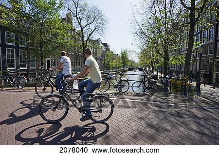 Stock Image - Cyclists On A Bridge Over Herengracht, Amsterdam, Netherlands. Fotosearch
