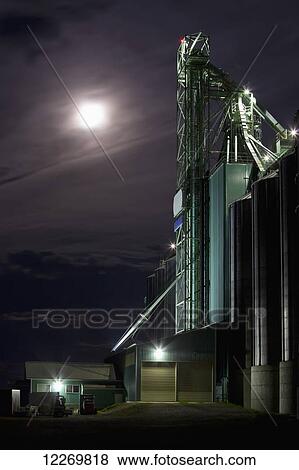 Stock Photo - Dark evening with moon behind clouds just prior to storm on the prairies next to a grain elevator; Alberta, Canada. Fotosearch