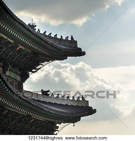 Stock Photograph - Detailed roofline of Gyeongbokgung Palace against a blue sky with cloud; Seoul, South Korea. Fotosearch