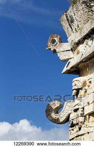 Stock Image - Detailed stone carvings on side of an ancient Mayan building with blue sky and clouds; Chichen Itza, Yucatan, Mexico. Fotosearch