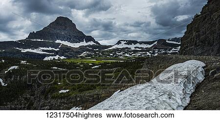 Stock Photograph - Dirty snow in a drift in the foreground with rugged cliffs and mountains in the background; Browning, Montana, United States of America. Fotosearch